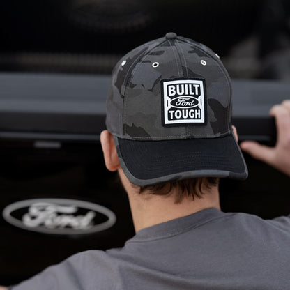 Person wearing a cap with 'Built Ford Tough' logo in front of a Ford vehicle.