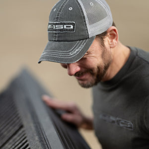 Man wearing a cap with 'F-150' logo, looking at a car part.
