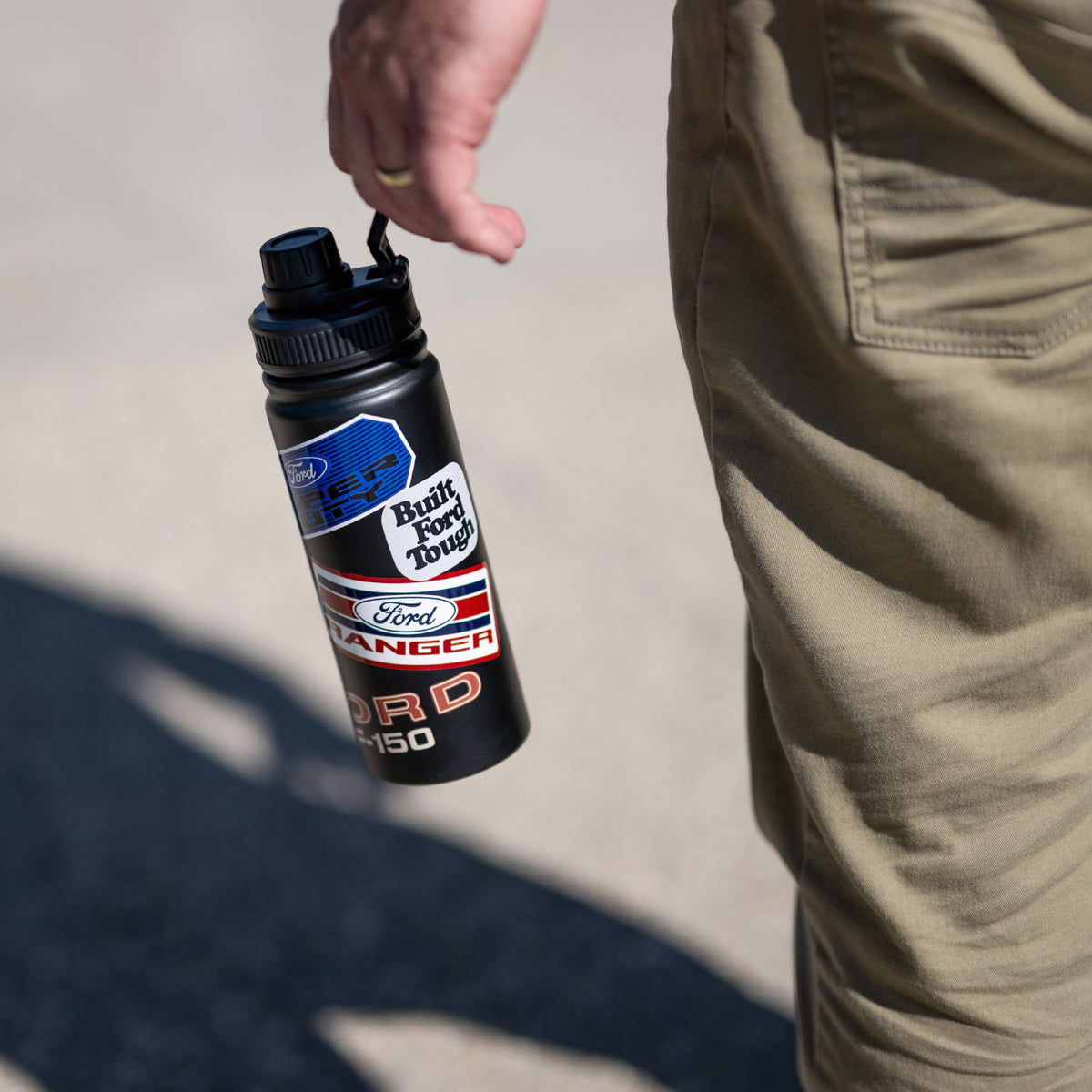 man holding a black Ford Trucks water bottle with patches on a cream background