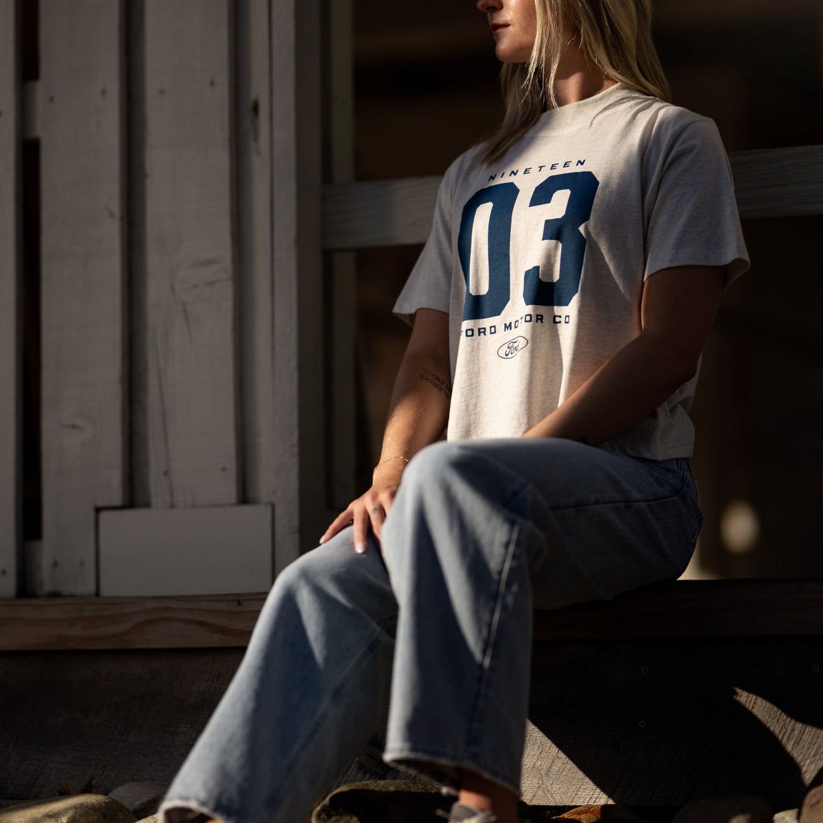 woman in a ford motor co t-shirt sitting outside on a barn step