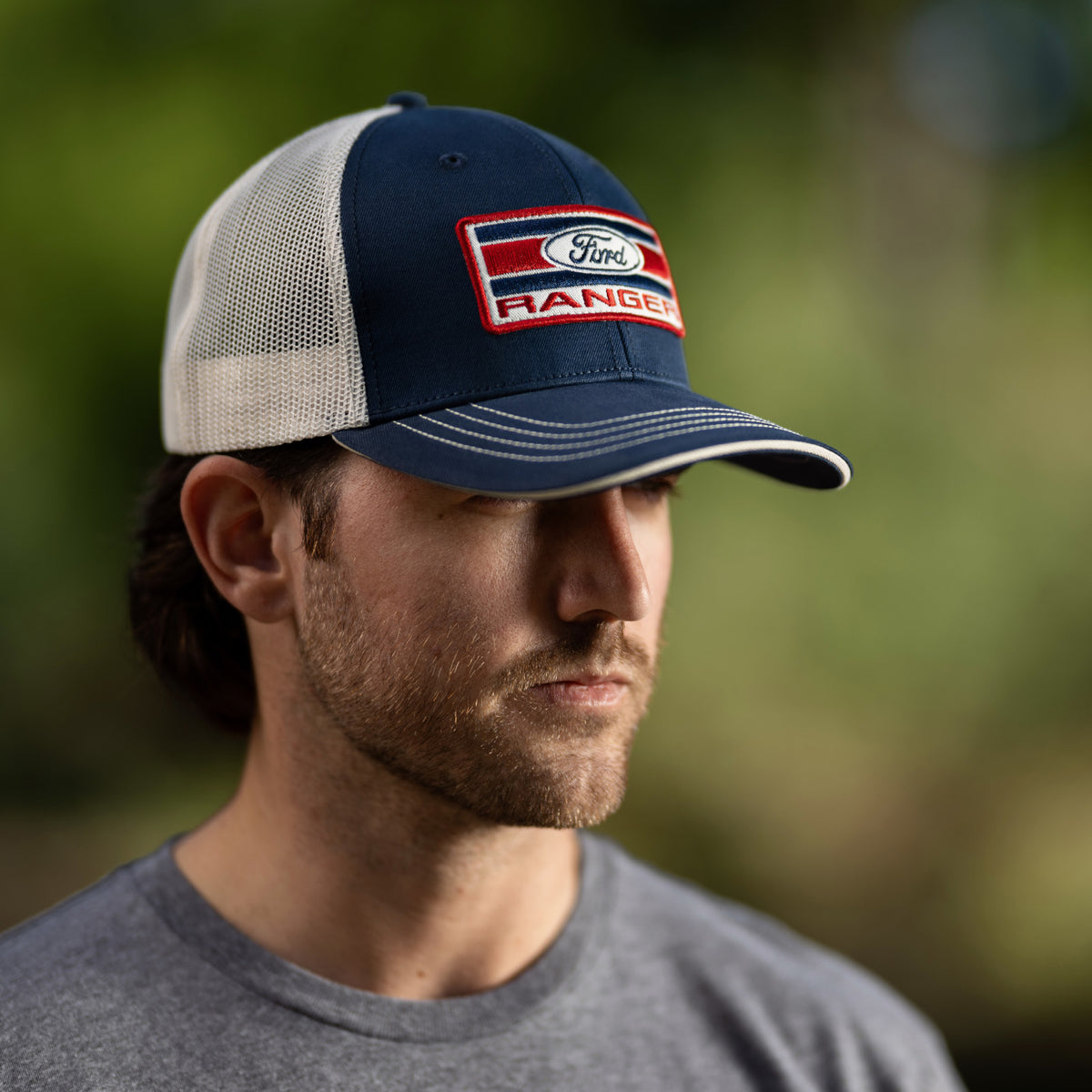 man in a gray ranger shirt wearing a navy blue hat with an americana ford ranger patch standing outside