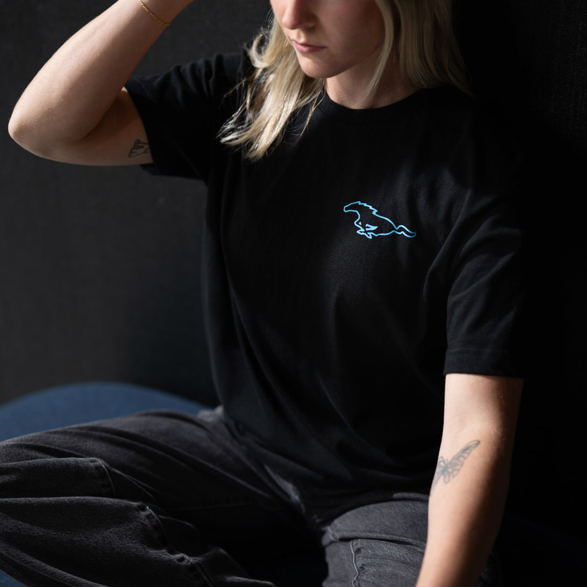 woman wearing a mustang mach-e t-shirt sitting on a bench on a black background