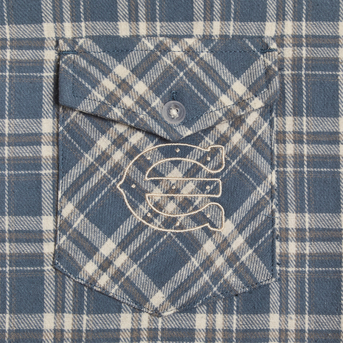 close up of an embroidered enchante  on a blue plaid button pocket