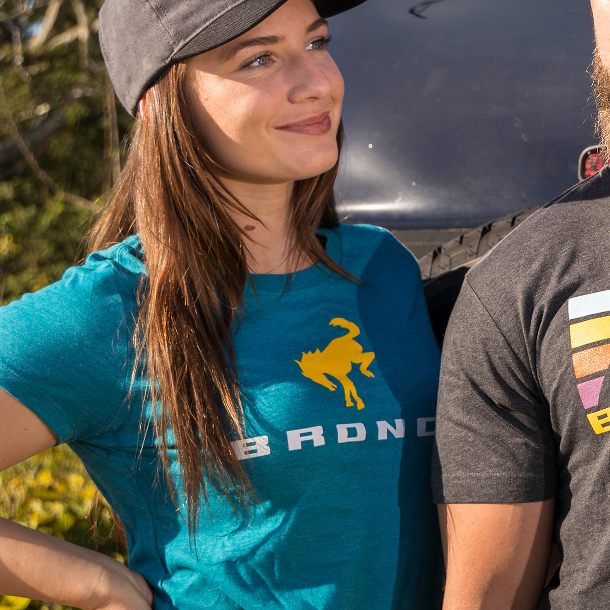 women wearing a teal bronco shirt smiling with a hat on