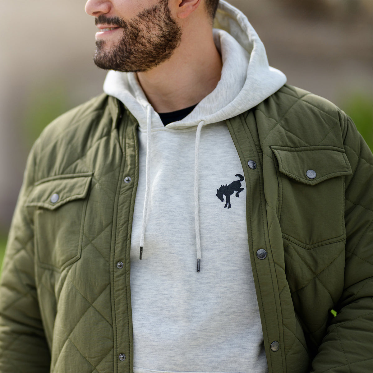 Man wearing a green quilted jacket over a white hoodie with a logo.