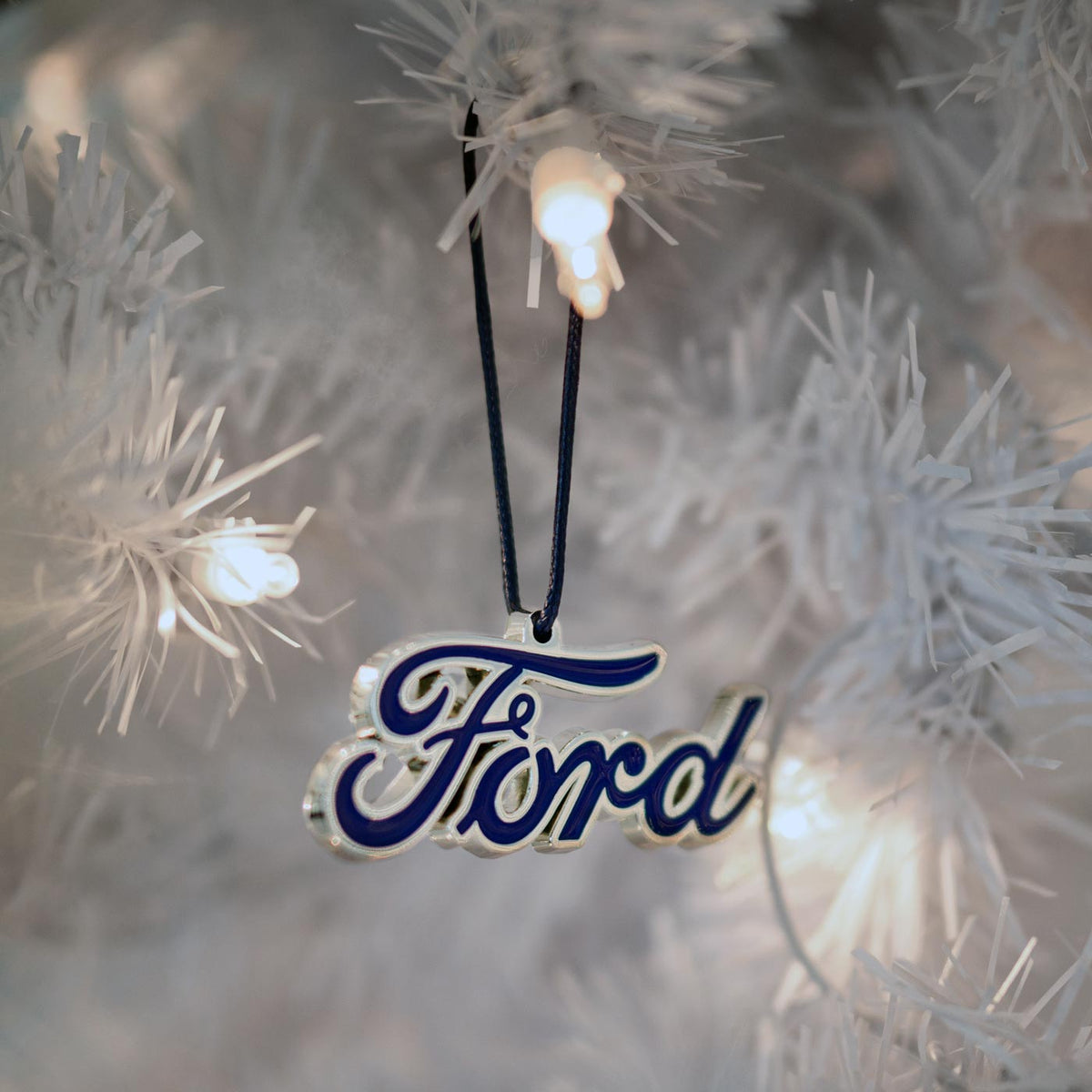 Ford logo ornament hanging on a Christmas tree with lights.
