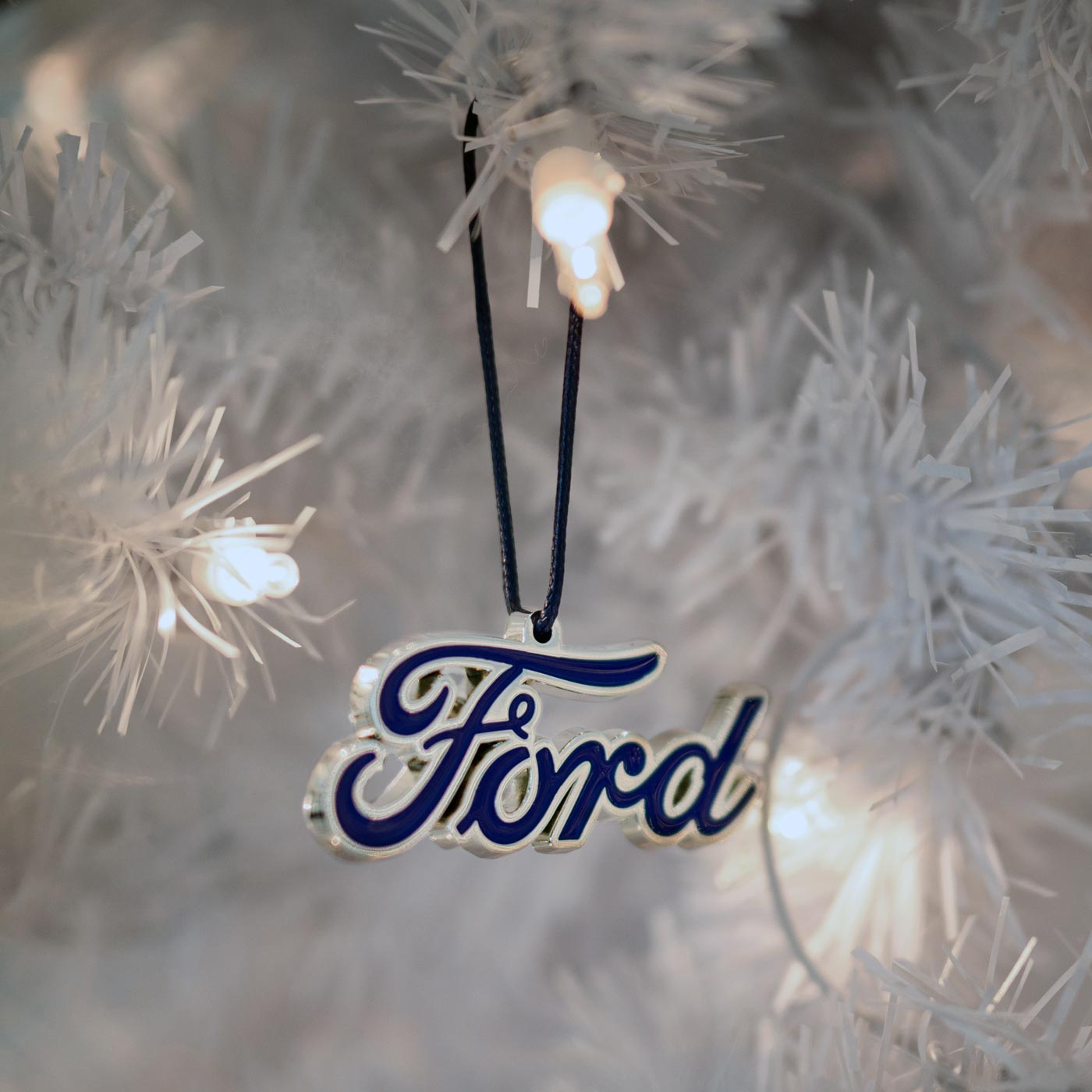 Ford logo ornament hanging on a Christmas tree with lights.