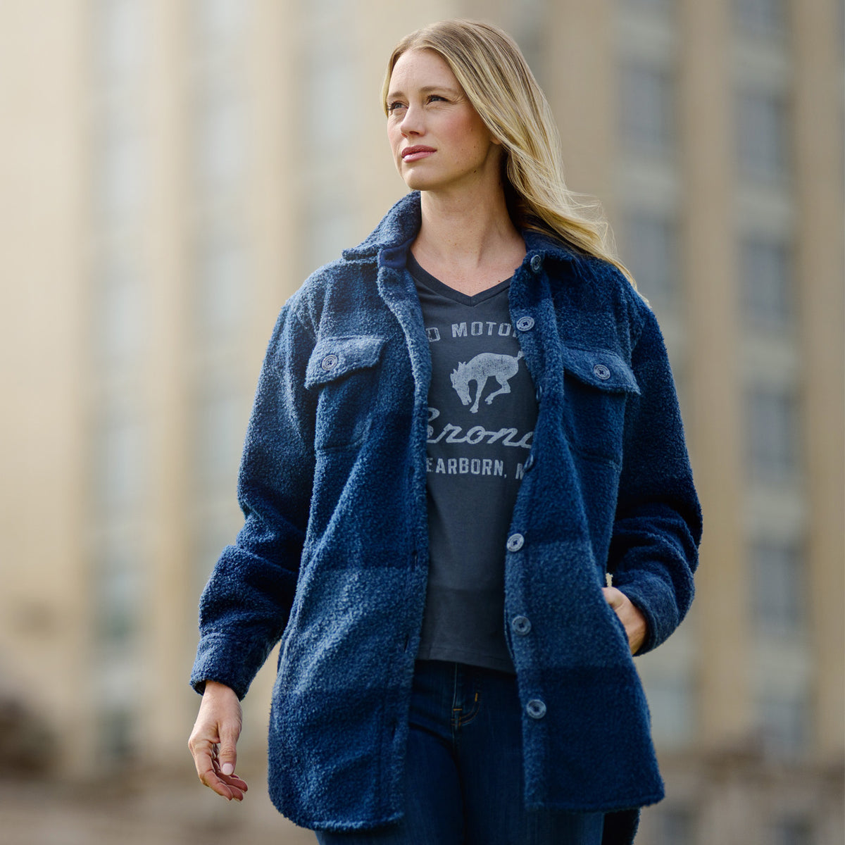 Woman wearing a blue jacket over a graphic t-shirt with a blurred cityscape background