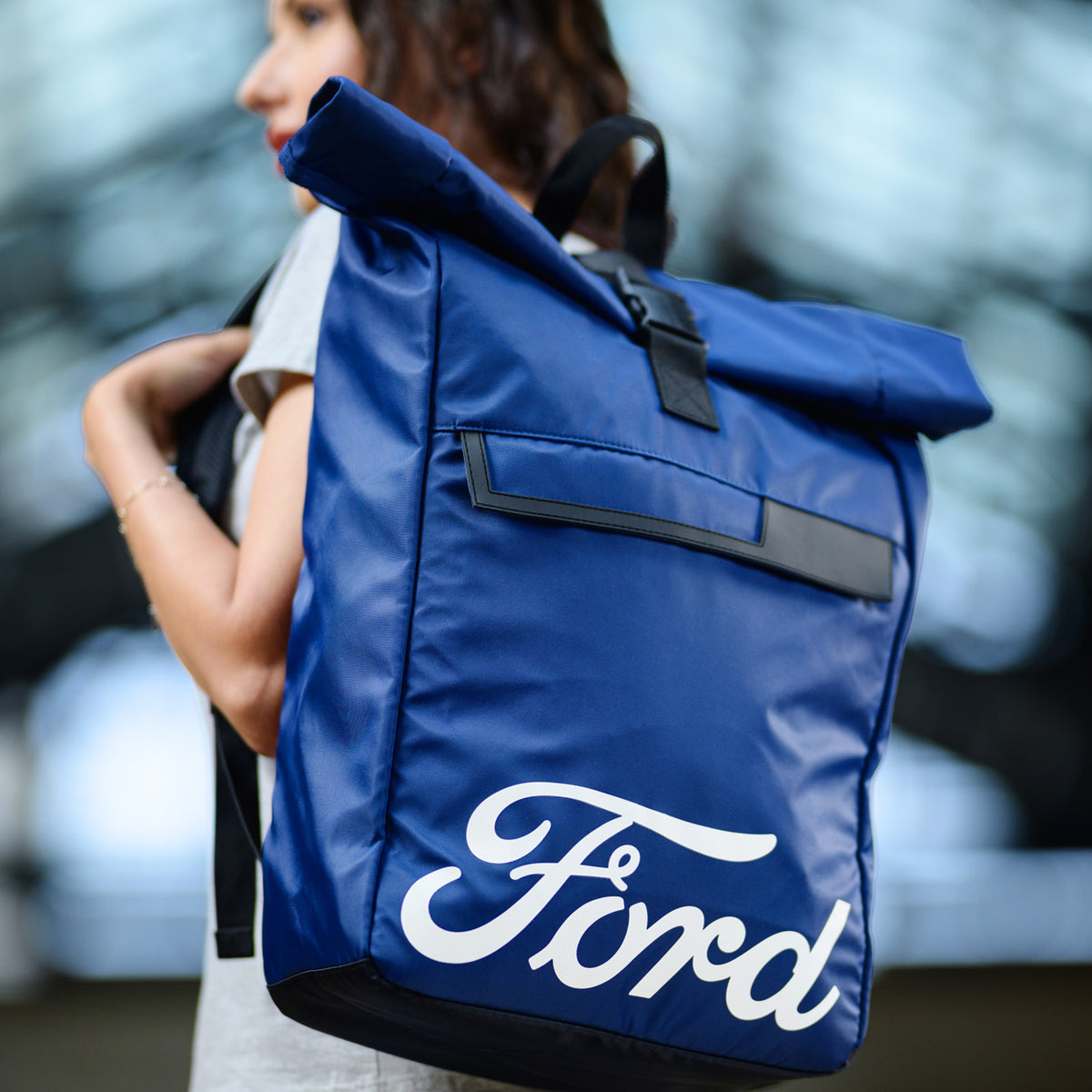 Person holding a blue backpack with 'Ford' branding against a blurred outdoor background