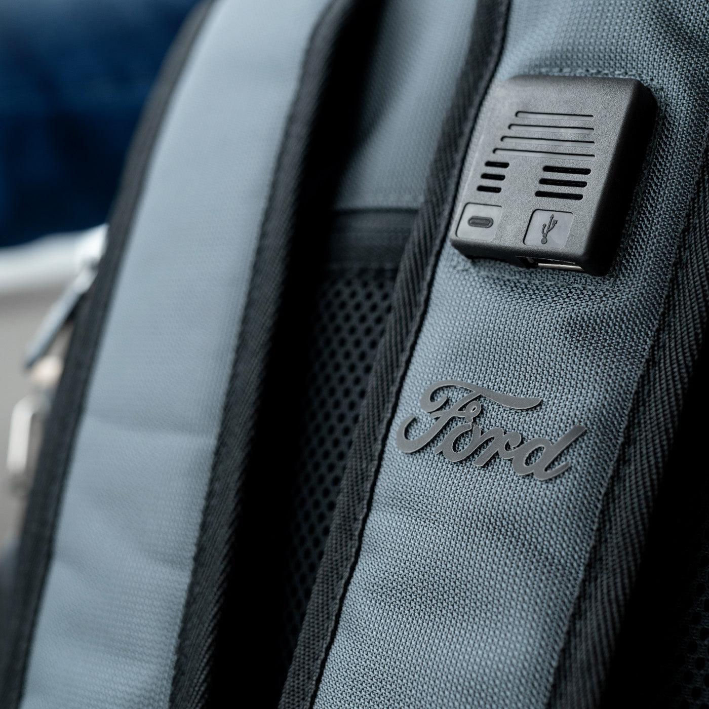 Gray backpack with Ford logo and USB port on a blurred outdoor background