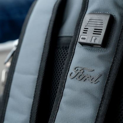 Gray backpack with Ford logo and USB port on a blurred outdoor background