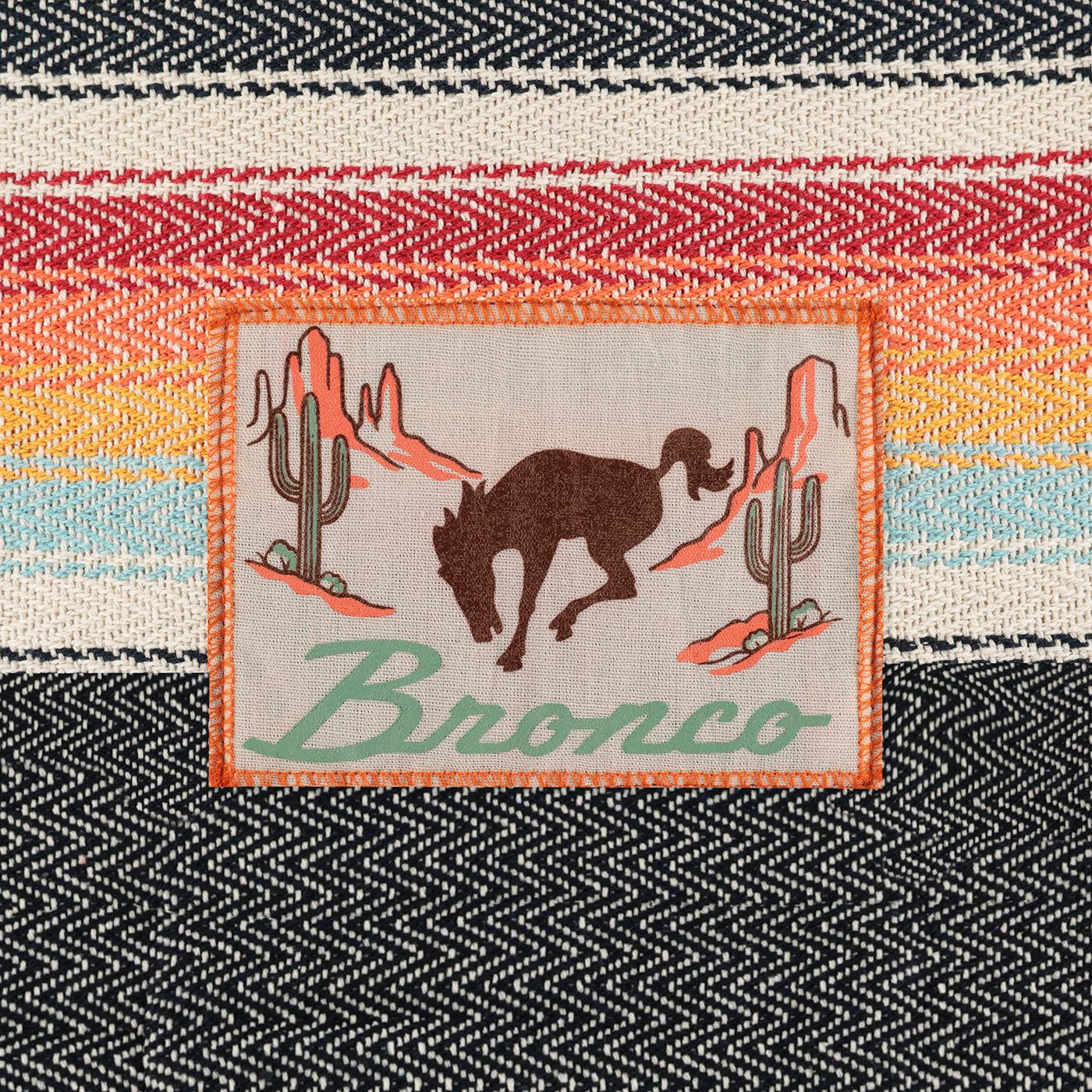Patch with a bronco and cactus design on a woven fabric background