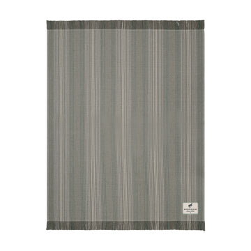 A rectangular woven rug with a vertical stripe pattern in shades of gray, beige, and white, featuring fringed edges and a small white brand label in the bottom right corner.