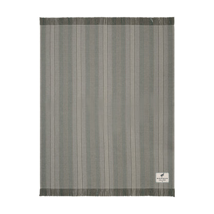 A rectangular woven rug with a vertical stripe pattern in shades of gray, beige, and white, featuring fringed edges and a small white brand label in the bottom right corner.