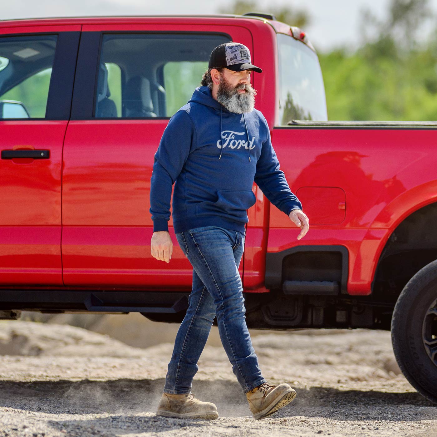 Man wearing a blue Ford hoodie walking next to a red truck outdoors.