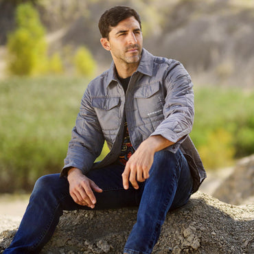guy looking into the distance sitting on rock wearing gray bronco quilted coat