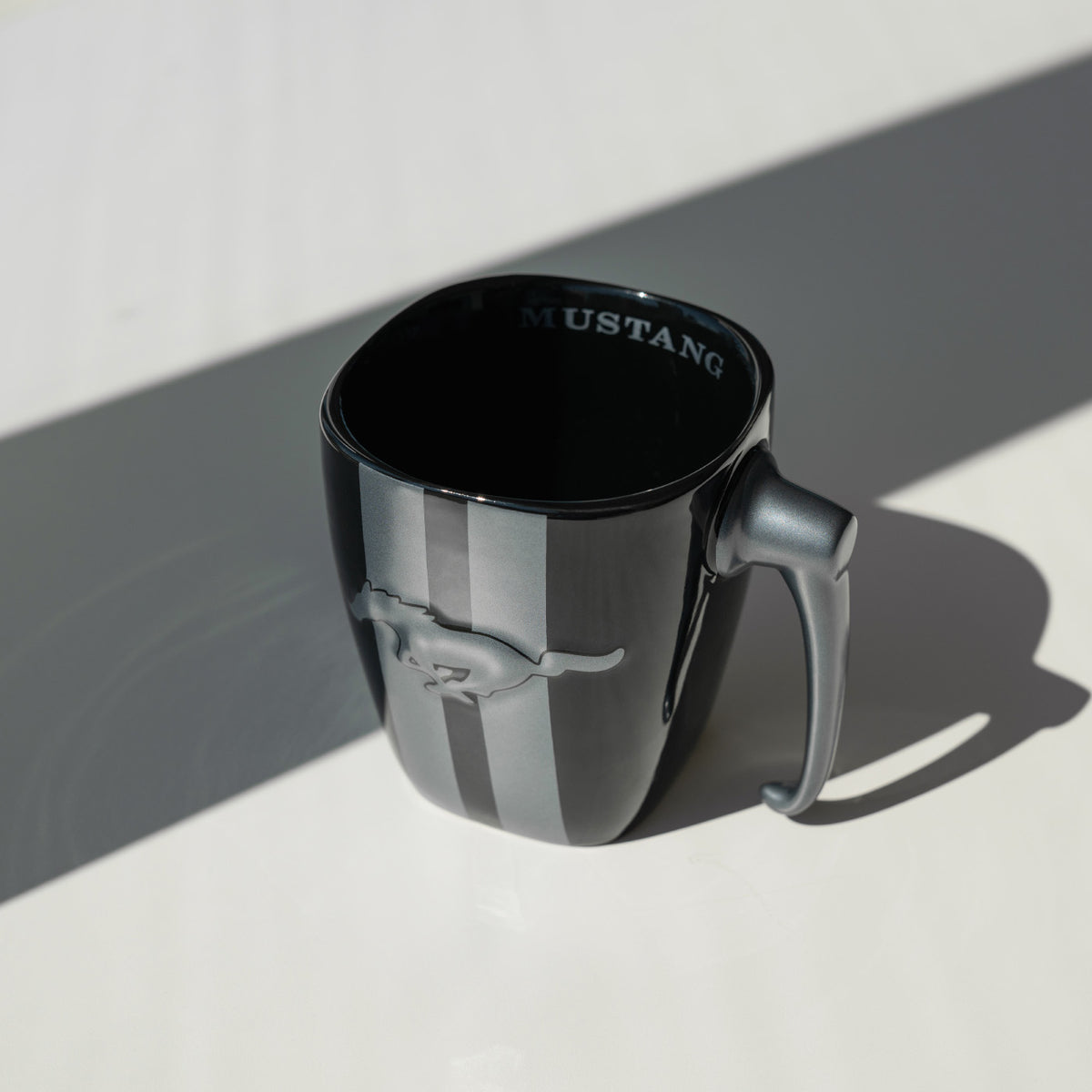 Black mug with silver stripes and pony logo with Mustang text and a gas pump handle sitting on a table