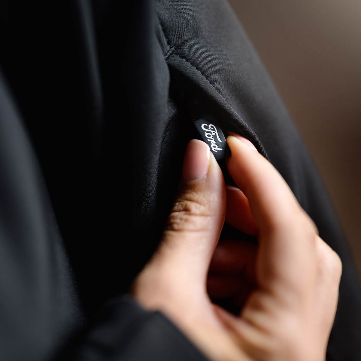 Hand holding a black jacket with a brand label against a blurred background