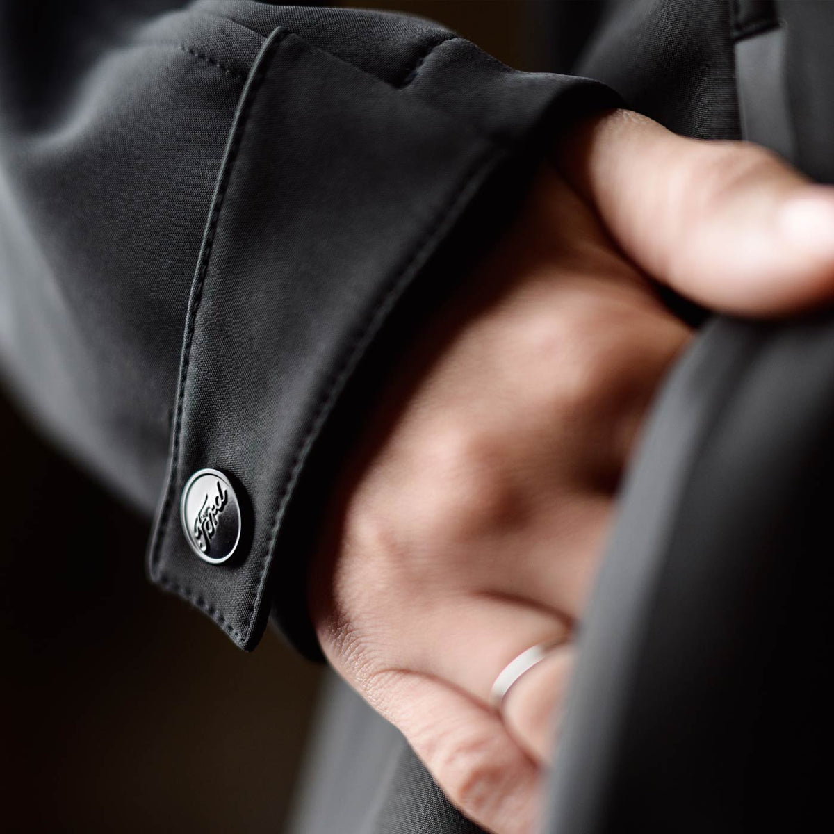 Close-up of a hand wearing a black jacket with a button, on a dark background