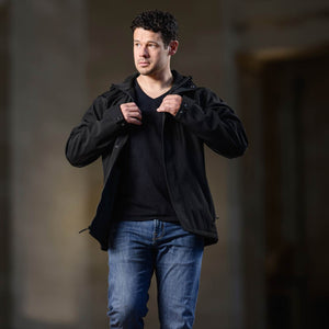 Man wearing a black jacket and blue jeans against a dark background