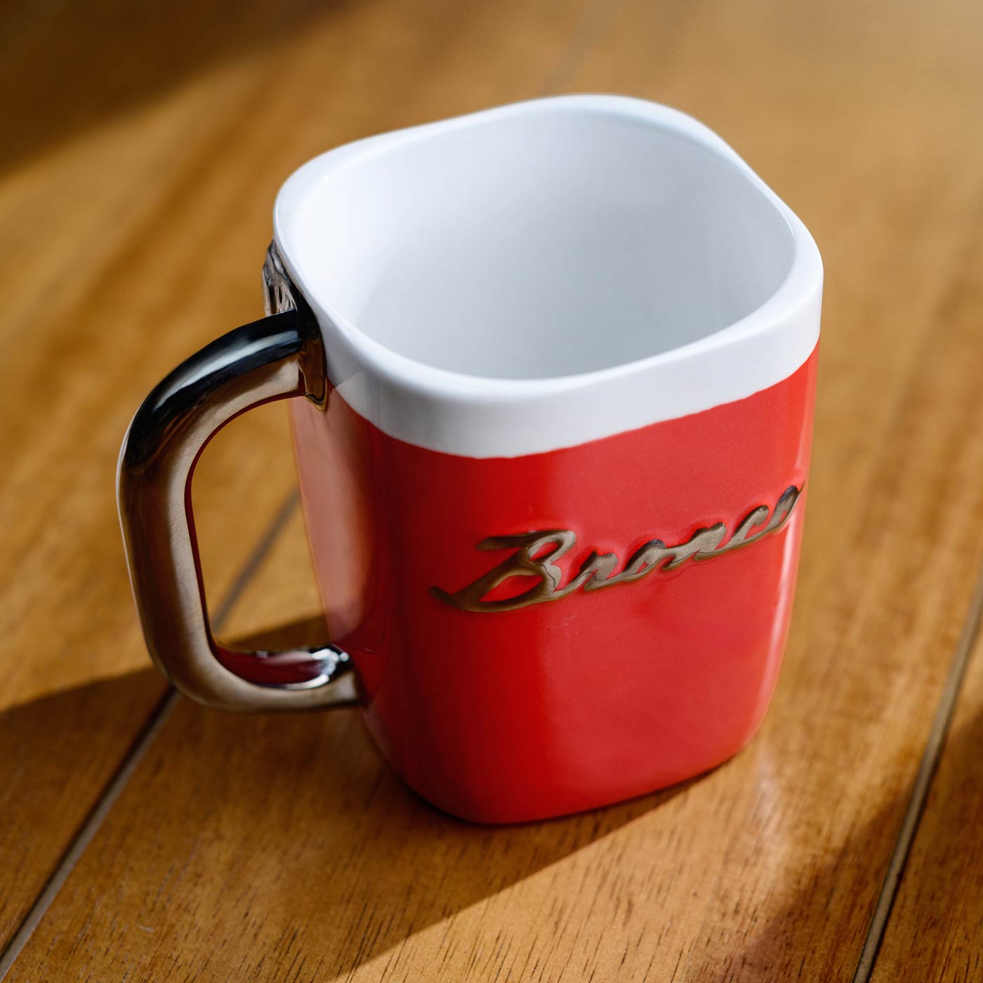 Red mug with white top and black handle on a wooden surface