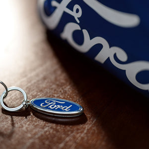 Ford keychain tag on a wooden surface with a blurred Ford logo in the background