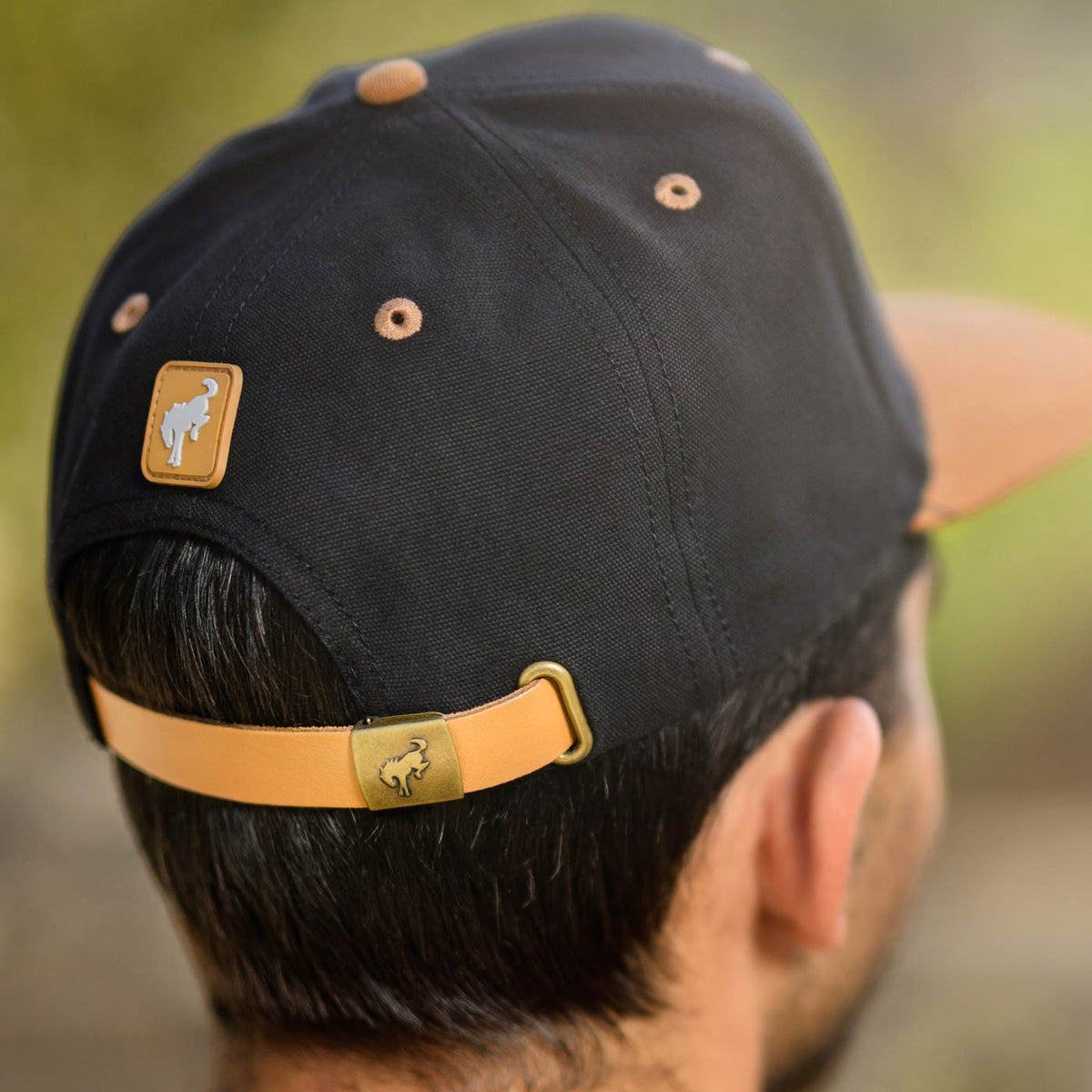man wearing a black bronco hat with a small tan bronco patch and bucking bronco on metal closure