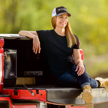 Woman sitting on a red truck bed wearing a black and white cap Ford hat and black shirt.