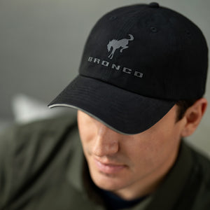 Person wearing a black cap with 'Bronco' logo on a gray background