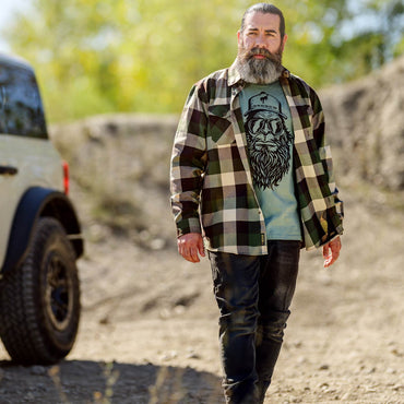 Man wearing a plaid shirt over a graphic t-shirt in an outdoor setting with a vehicle in the background.