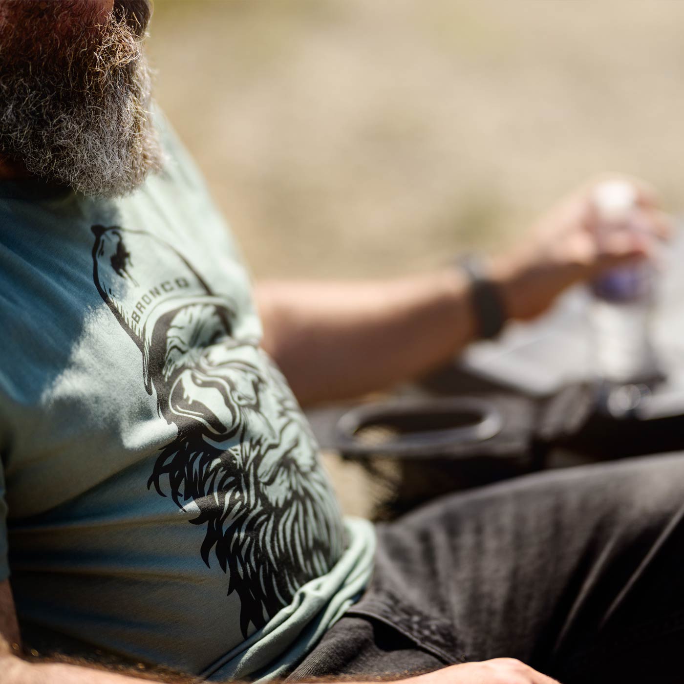 Person sitting outdoors holding a water bottle, wearing a graphic t-shirt.