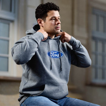 Man wearing a gray hoodie with a Ford logo, sitting outdoors.
