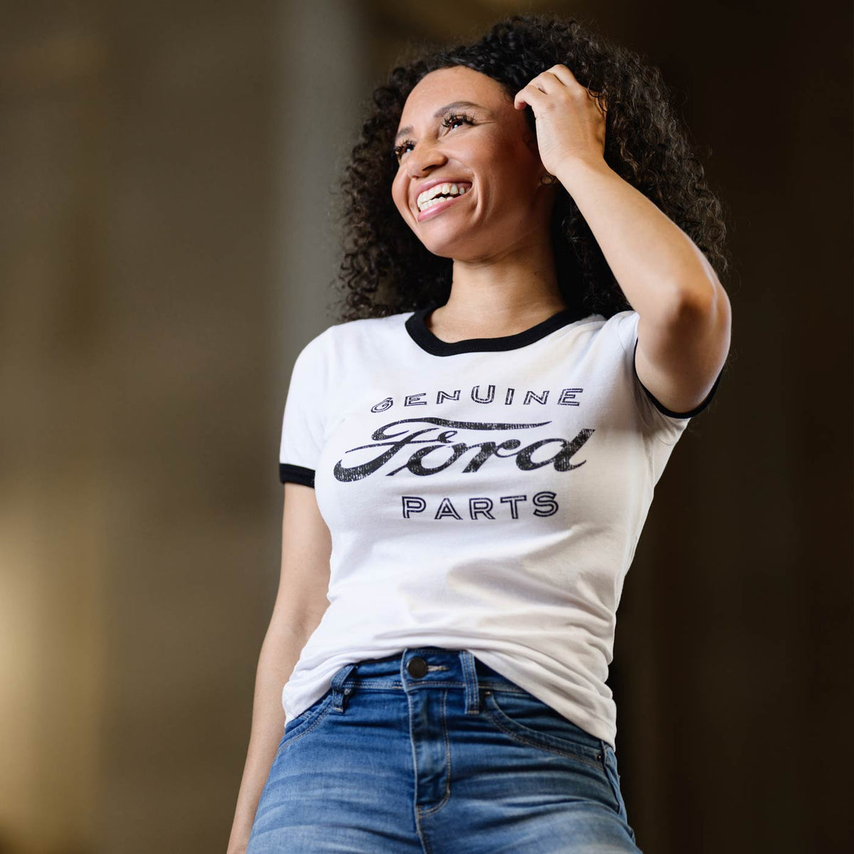 Woman wearing a white t-shirt with 'Genuine Ford Parts' text, standing against a dark background.