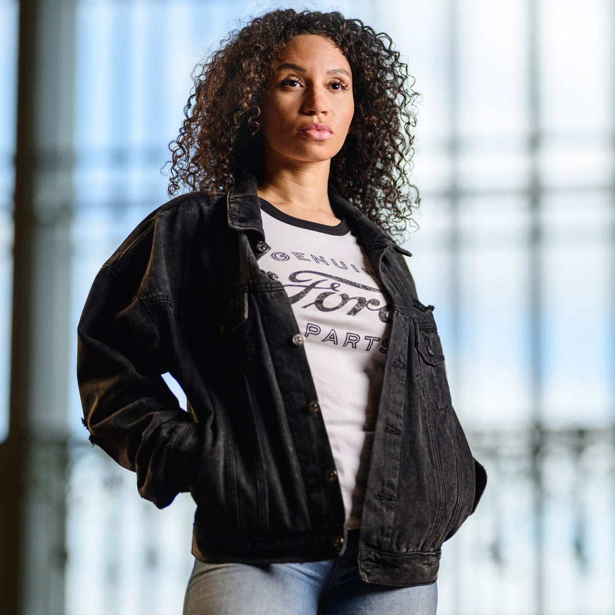 Woman wearing a black jacket over a white t-shirt with text, standing indoors.