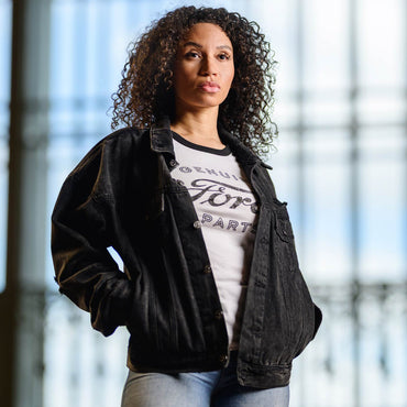 Woman wearing a black jacket over a white t-shirt with text, standing indoors.
