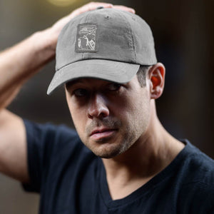 Man wearing a gray cap with a logo, adjusting it on his head.