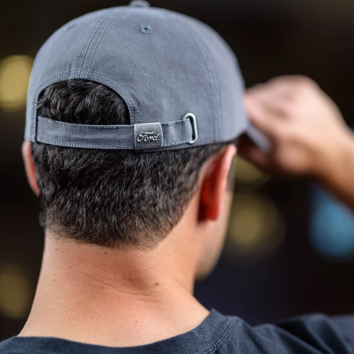 Person wearing a gray cap with a Ford logo on the back, against a blurred background.