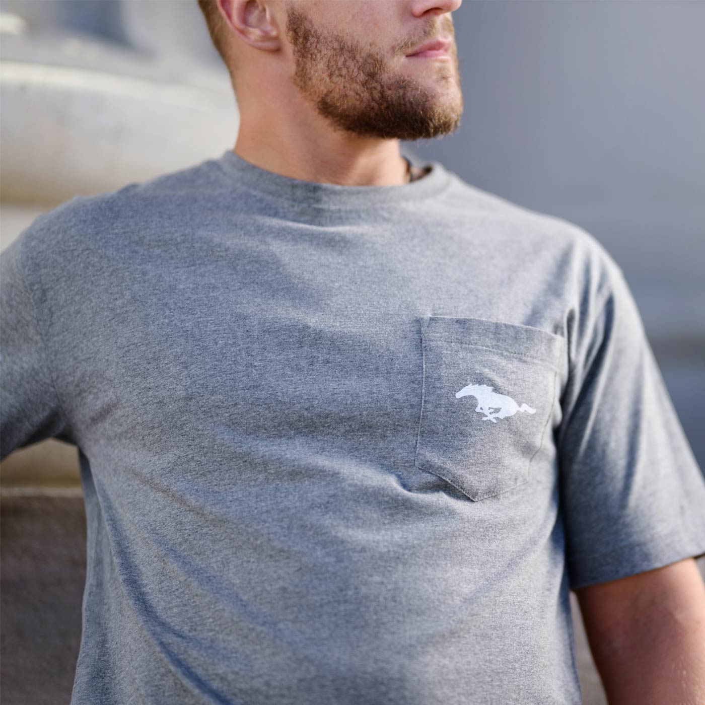 Man wearing a gray t-shirt with a mustang pony logo on the chest, standing outdoors.