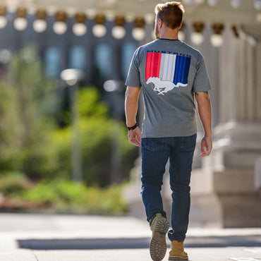 Man walking outdoors wearing a gray t-shirt with a colorful mustang tribar logo graphic on the back.