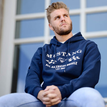 Man wearing a navy blue hoodie with vintage 'Mustang' branding, sitting outdoors.
