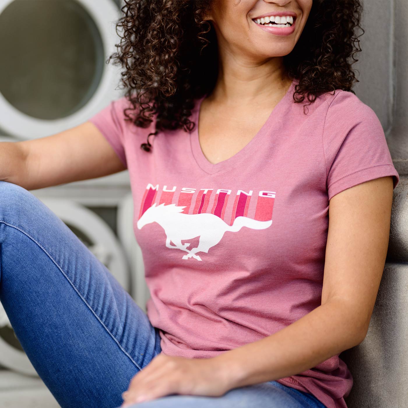 Woman wearing a pink t-shirt with a horse graphic and 'Mustang' text, sitting on a couch.
