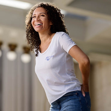 Woman wearing a white mustang mach-e t-shirt with a logo, standing indoors.