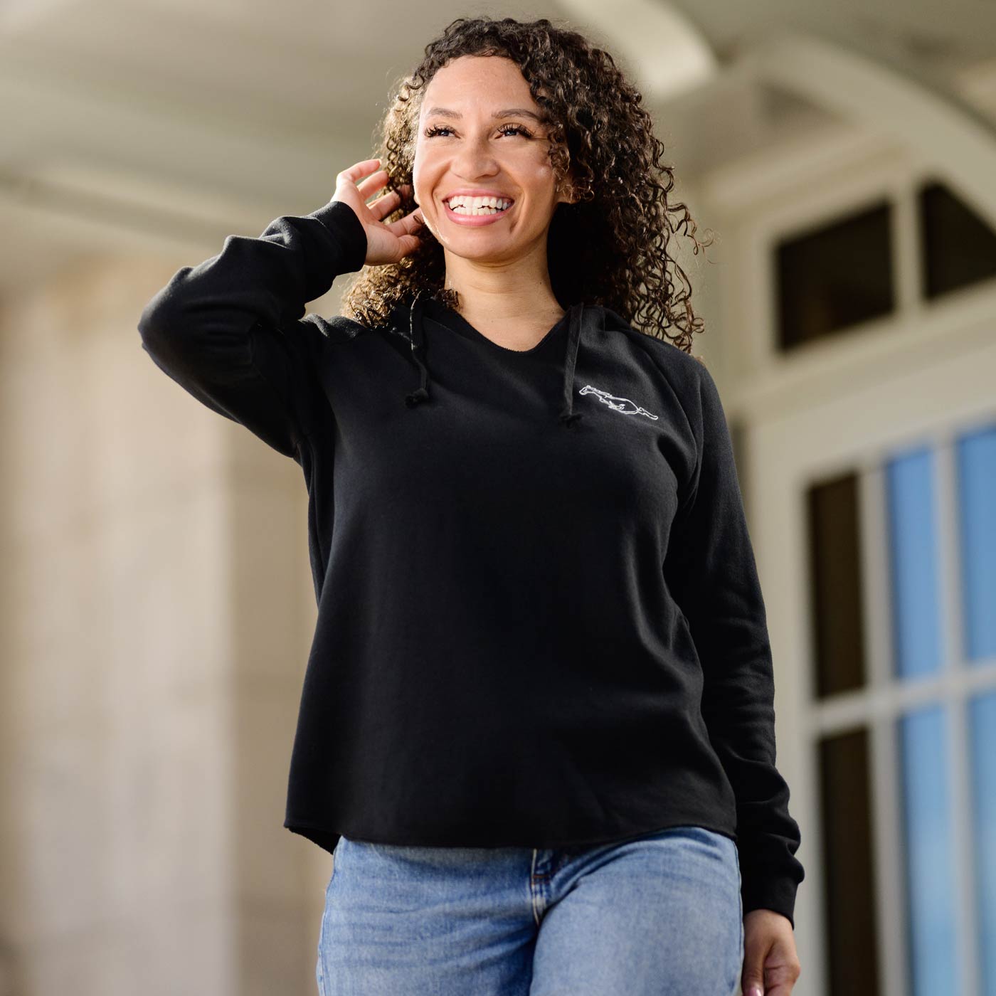 Woman wearing a black mustang sweatshirt with a logo, standing outdoors.
