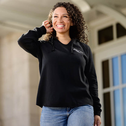Woman wearing a black mustang sweatshirt with a logo, standing outdoors.