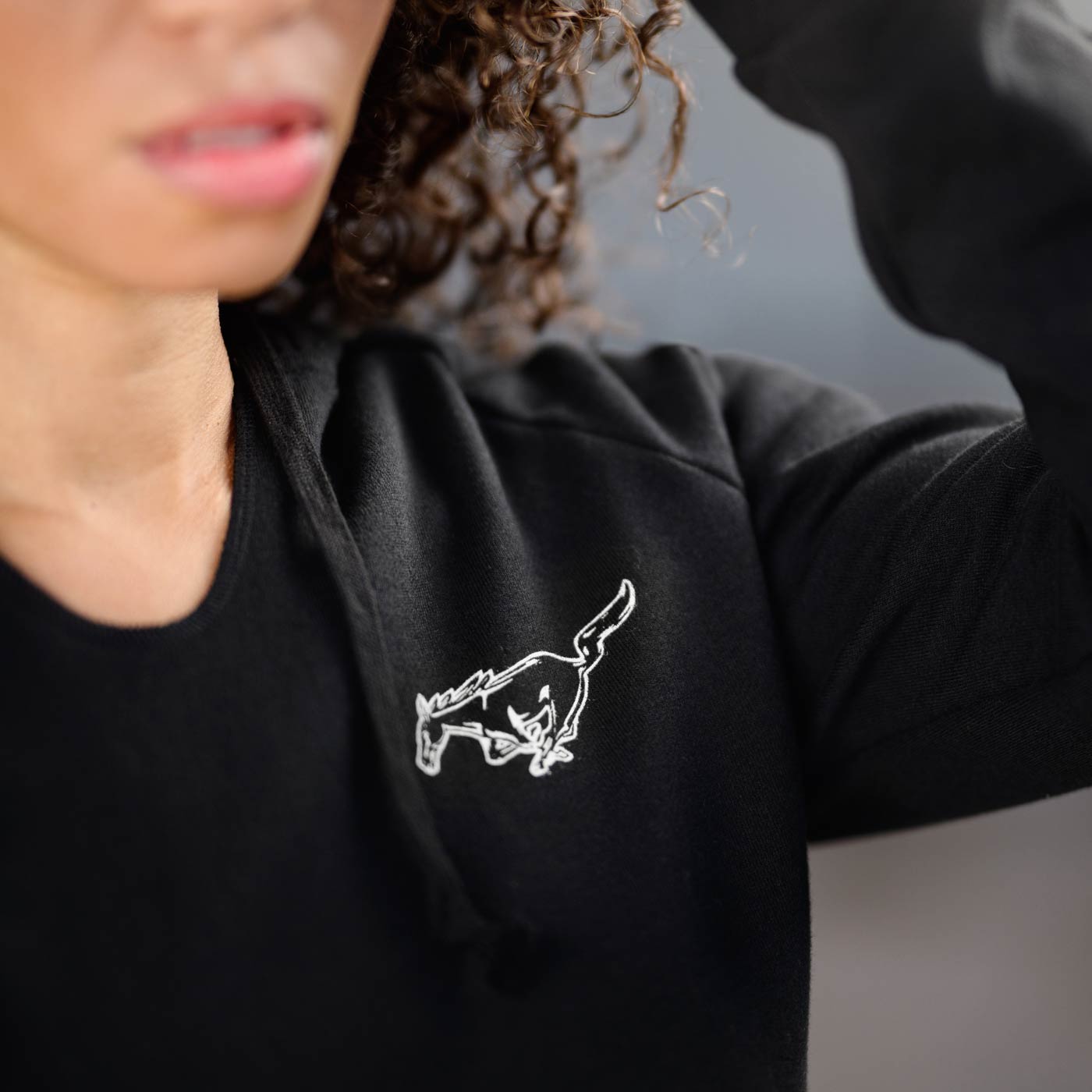 Person wearing a black hoodie with a white embroidered mustang design on a blurred background