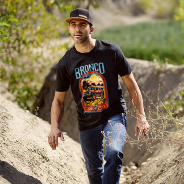 Man wearing a black t-shirt with 'Bronco' logo walking outdoors.