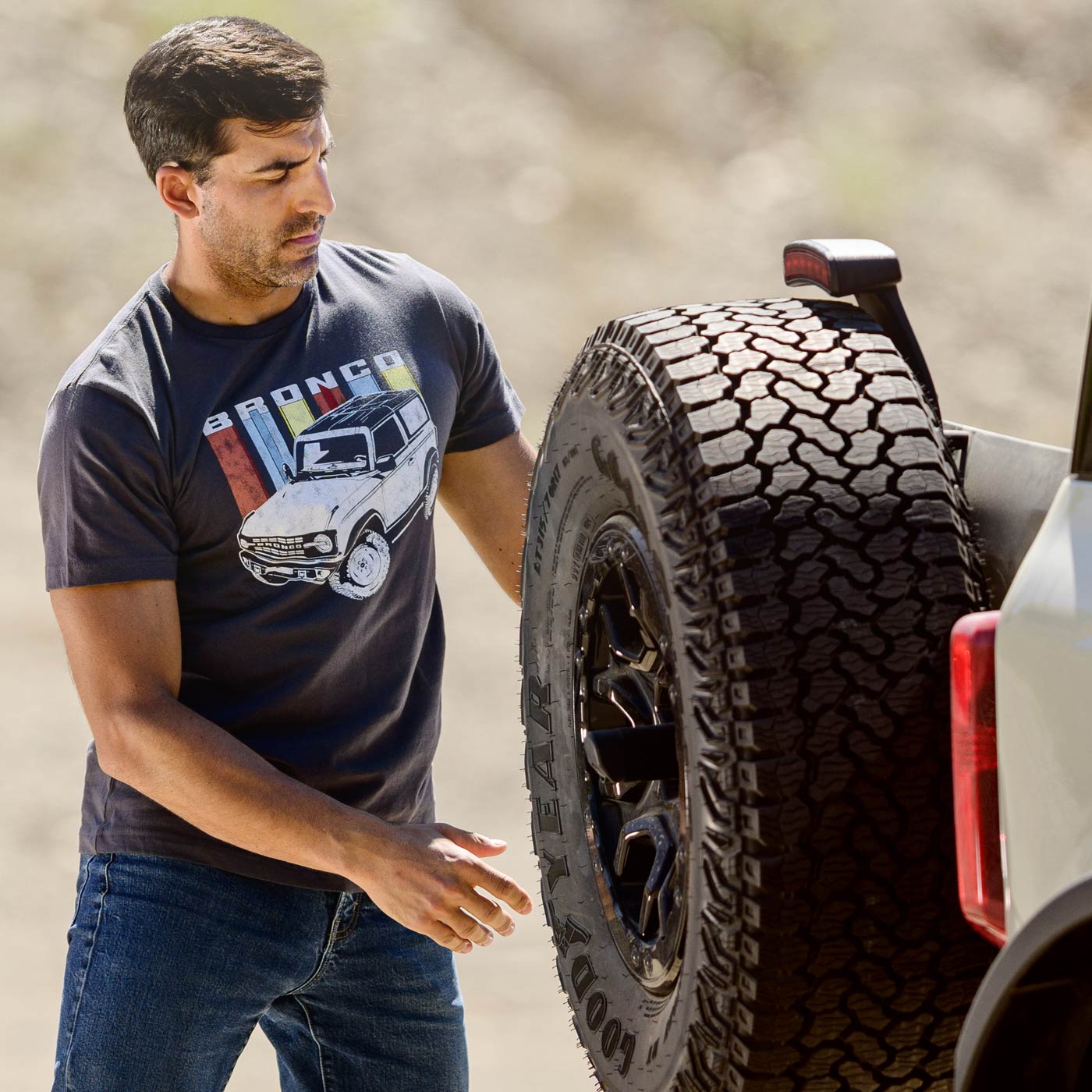 Man wearing a Ford Bronco t-shirt next to a vehicle with large off-road tires.