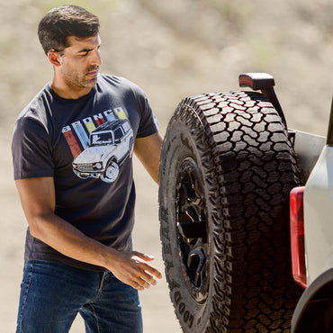 Man wearing a Ford Bronco t-shirt next to a vehicle with large off-road tires.
