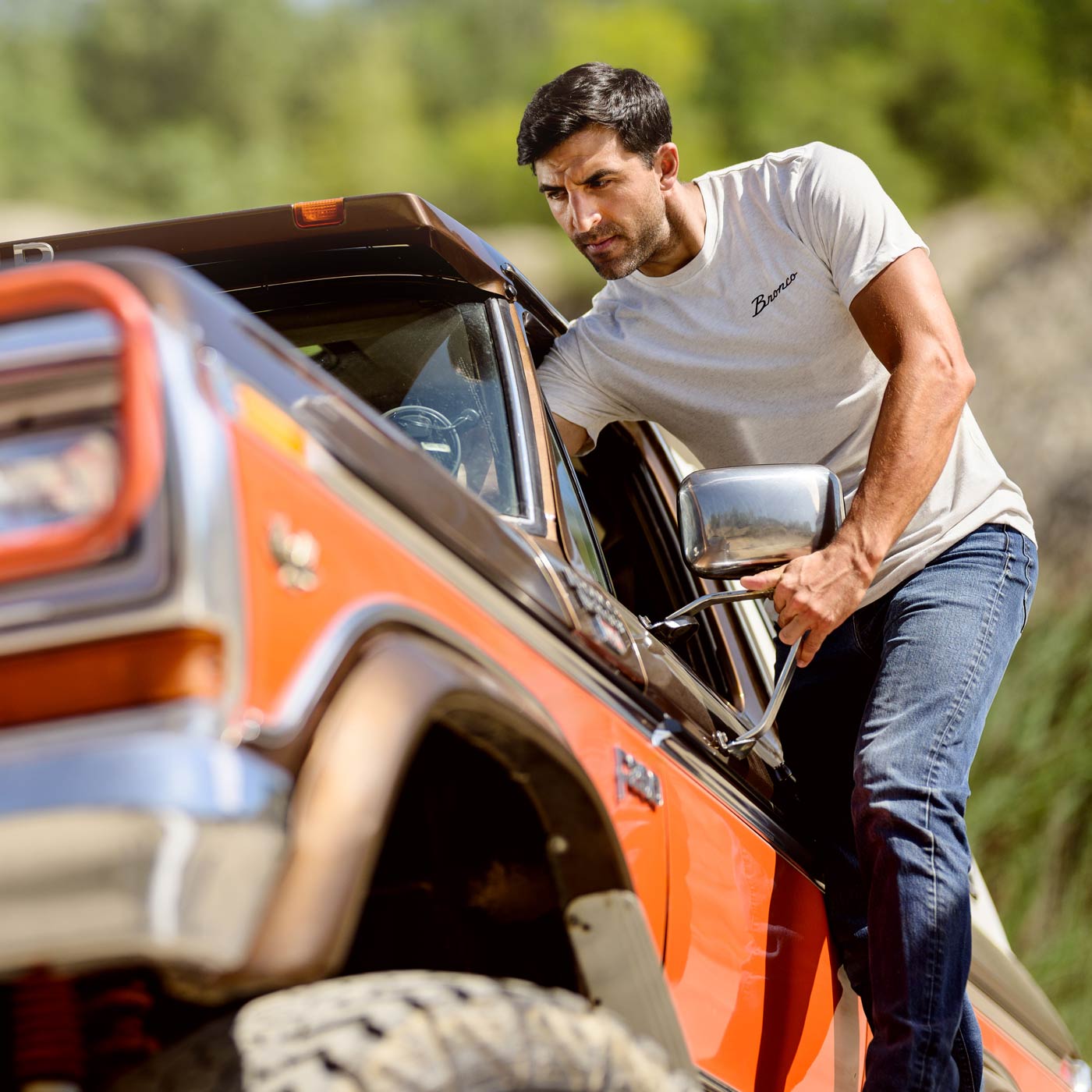 Man climbing out of an orange off-road vehicle with a blurred natural background