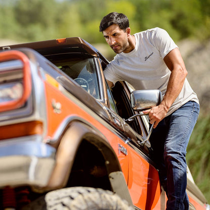 Man climbing out of an orange off-road vehicle with a blurred natural background